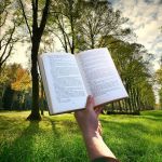image of a hand and arm holding an open book in front of some trees